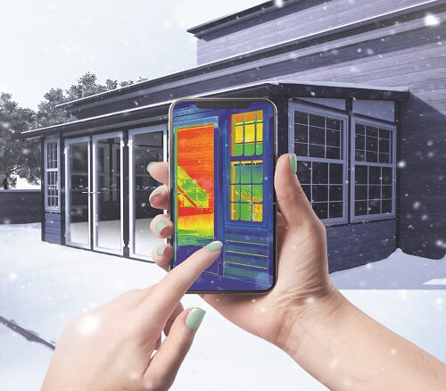 The exterior of a sunroom in the snow with hands holding a cellphone in the foreground showcasing the thermal temperature inside.