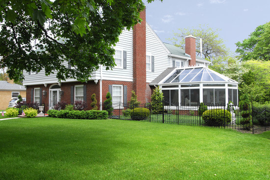 A Victorian conservatory connected to a brick home with a bright green lawn. 